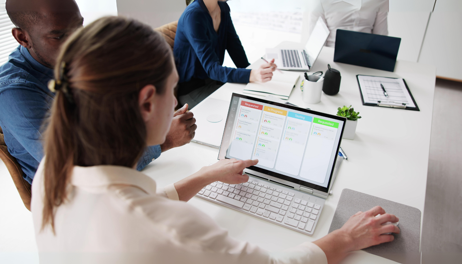 A team collaborates around a computer, pointing at a PPM software interface on the screen, discussing project plans and resource allocation